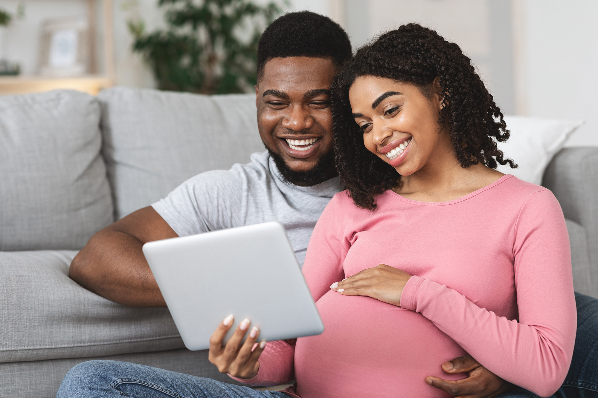 Pregnant african couple having fun at home, using digital tablet together, watching funny videos, empty space, closeup