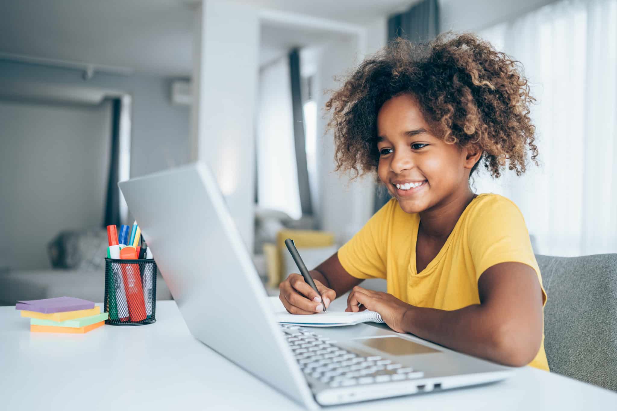Young girl sitting at a laptop and taking notes.
