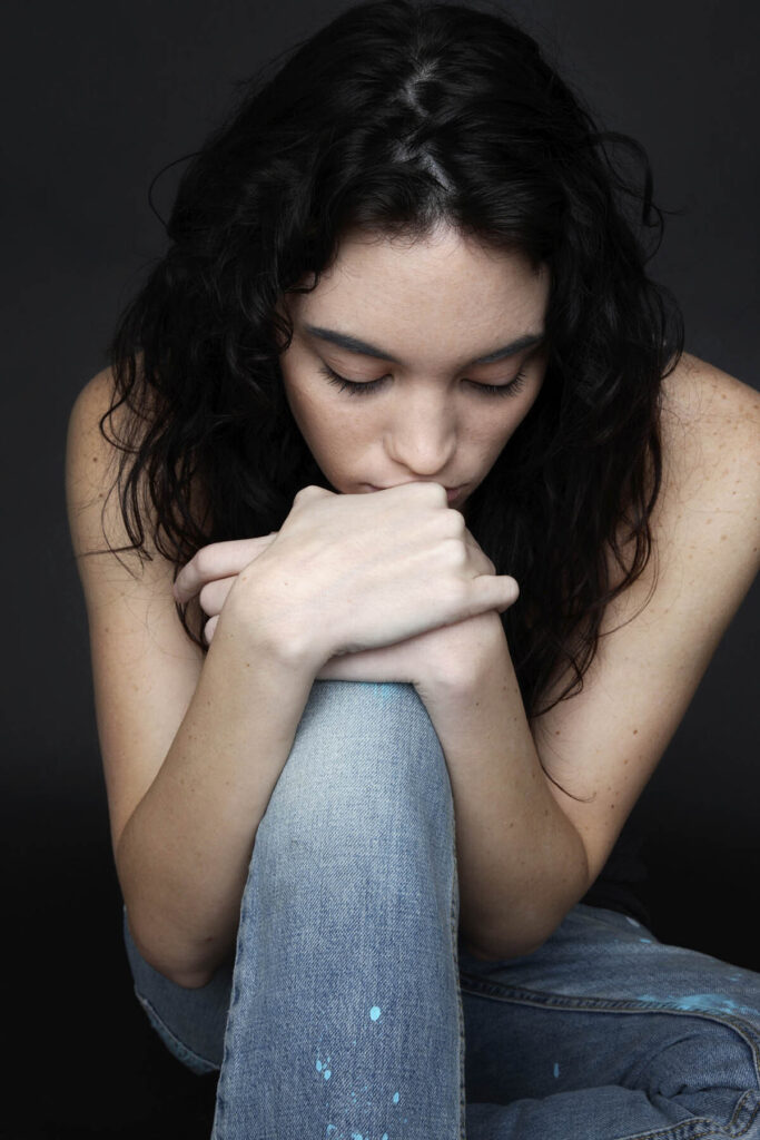 Dark haired teen in jeans with eyes closed thinking and kneeling