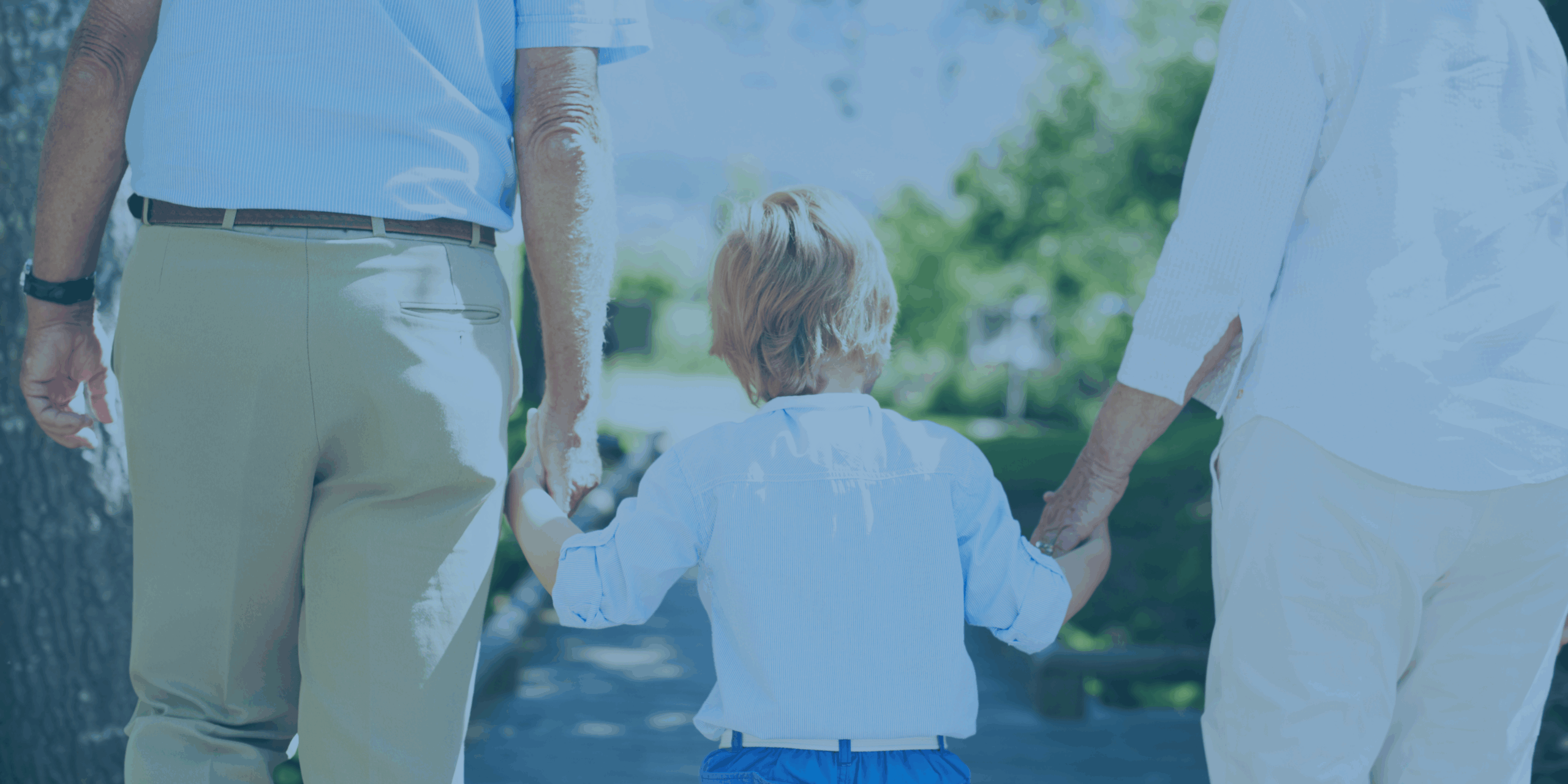 **Alt text:** An older adult couple walks hand-in-hand with a young child outdoors on a sunny day, symbolizing legacy and support across generations.